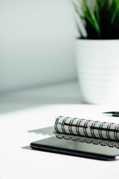 A phone and notebook resting on a white desk