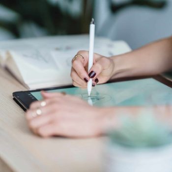 Womans's hands illustrating on a tablet using a pencil.