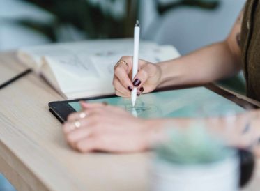 Womans's hands illustrating on a tablet using a pencil.