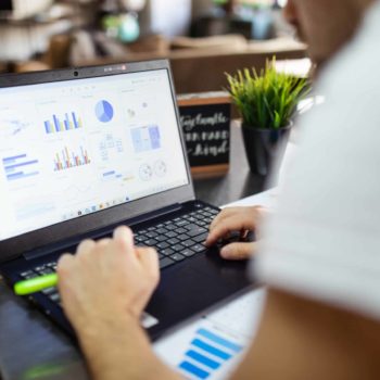 Man working on a laptop showing data visualizations as graphs.